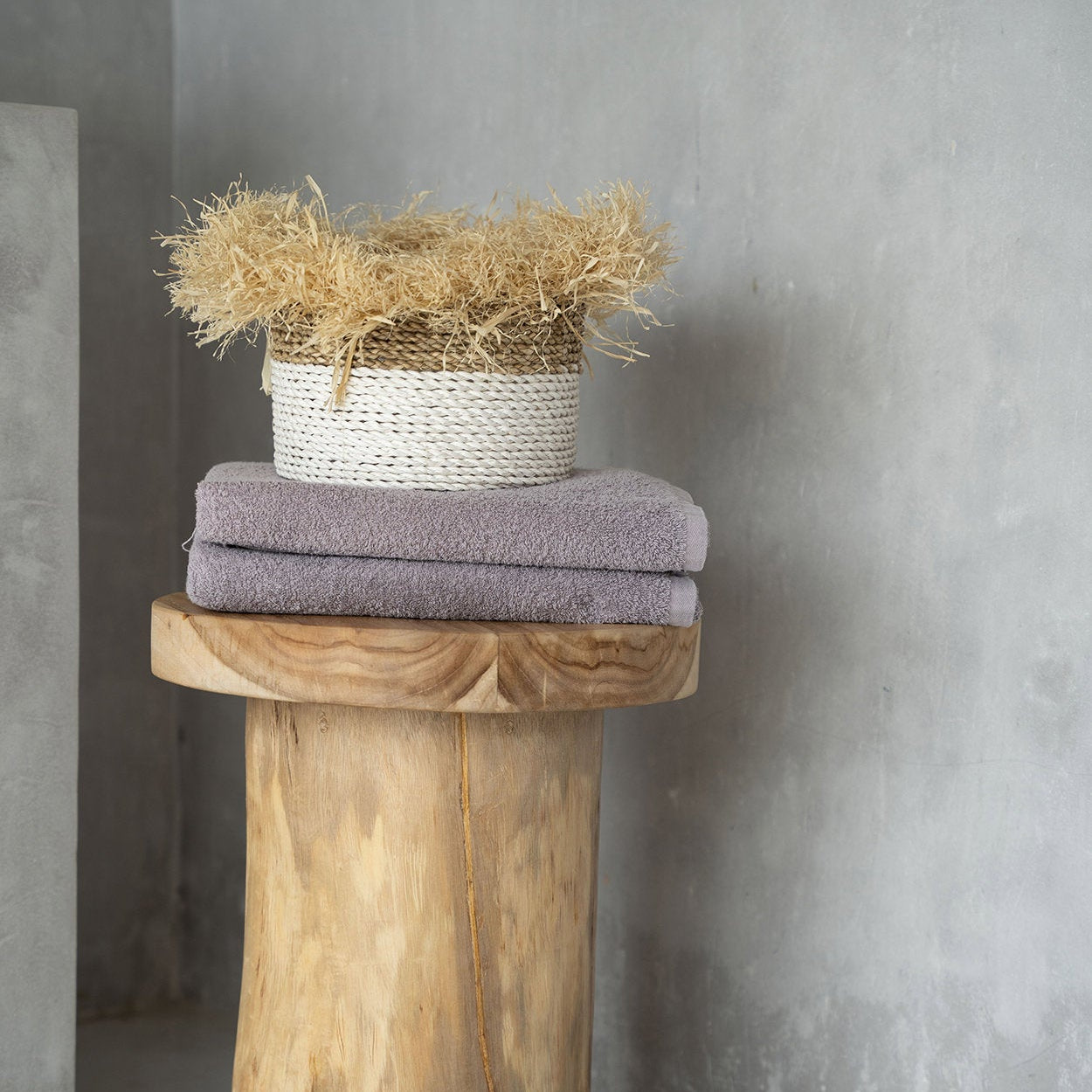 Wooden side table with towels and a basket against a concrete wall