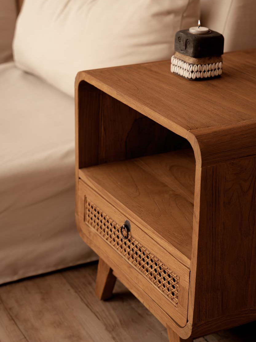 Wooden beside table with a candle near a beige bed.