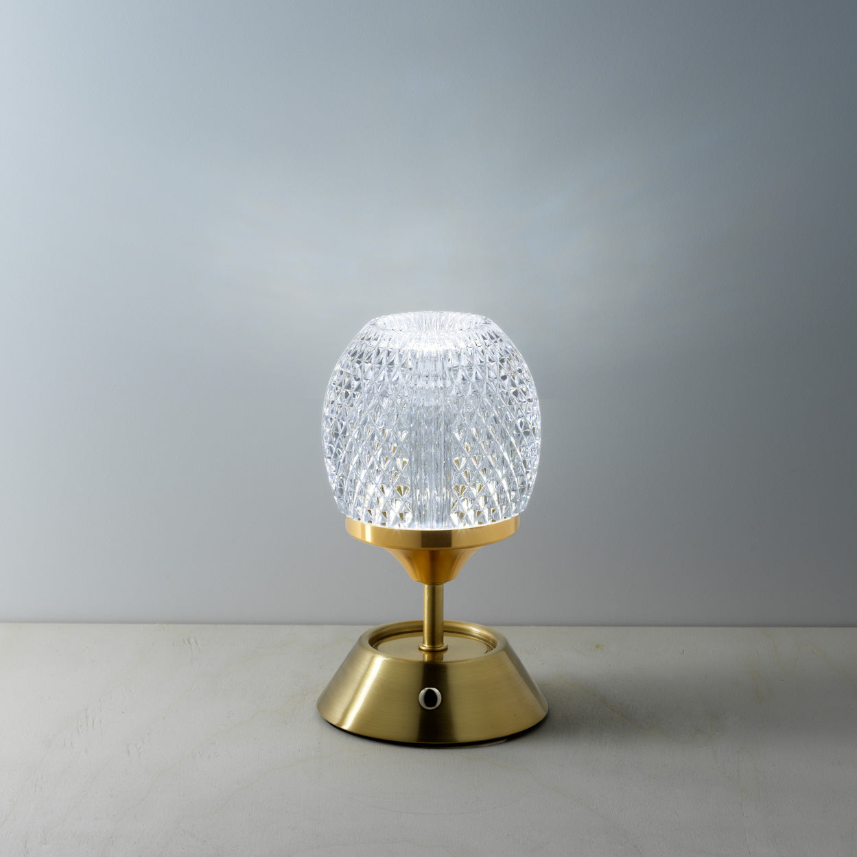 Table lamp with gold base and textured glass shade on a gray background