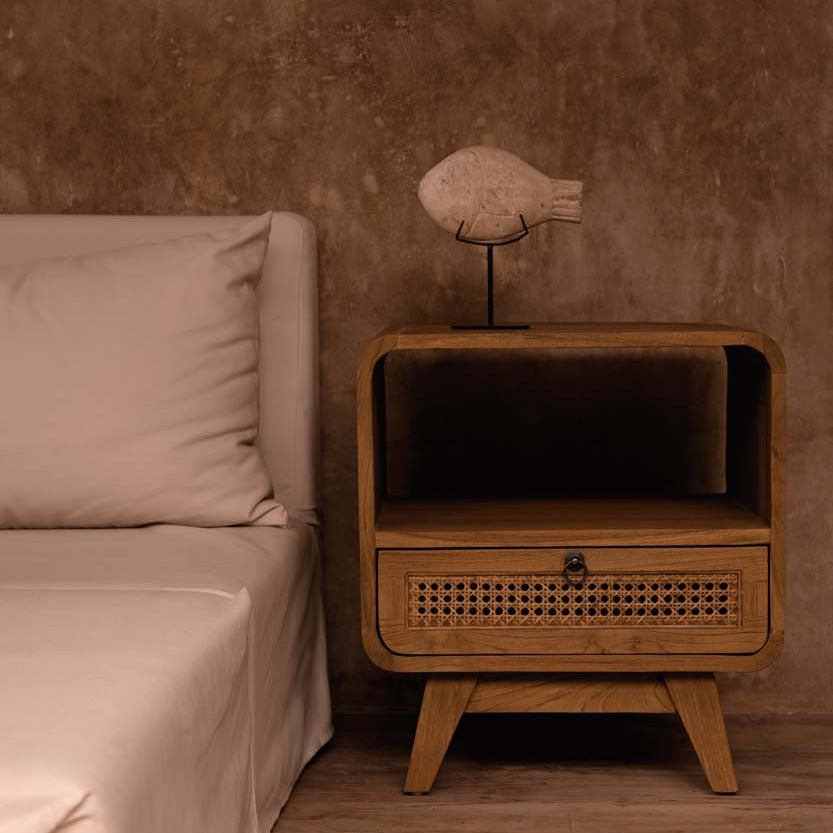 Wooden side table with a stone fish on stand next to a bed in a bedroom setting
