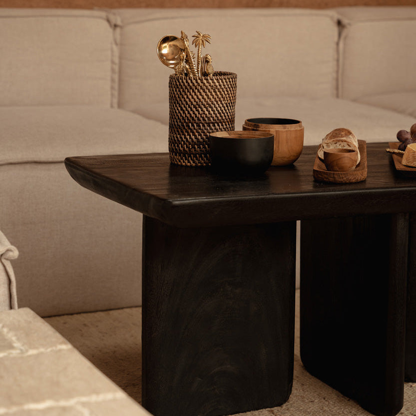 Black wooden coffee table with decorative items against a beige sofa and wall.