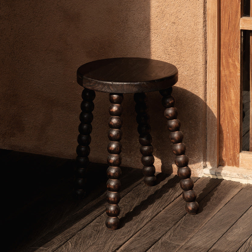 Wooden stool with against a textured wall.