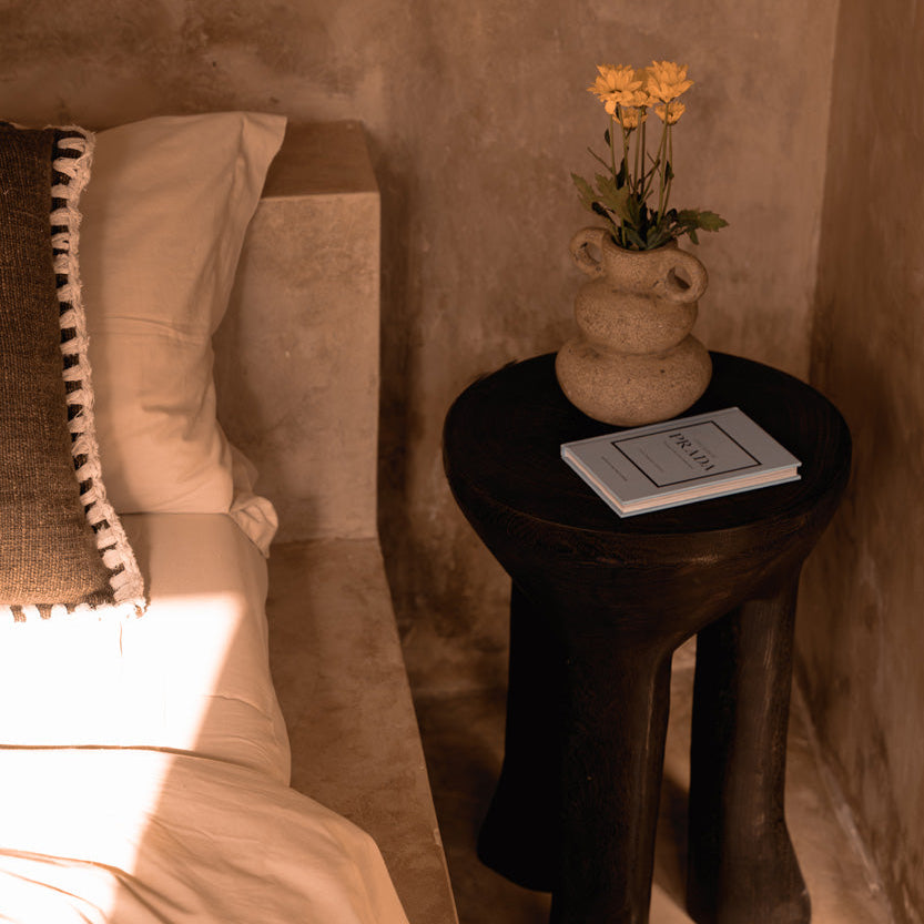 Small wooden side table with a vase of flowers and a book against a textured wall.