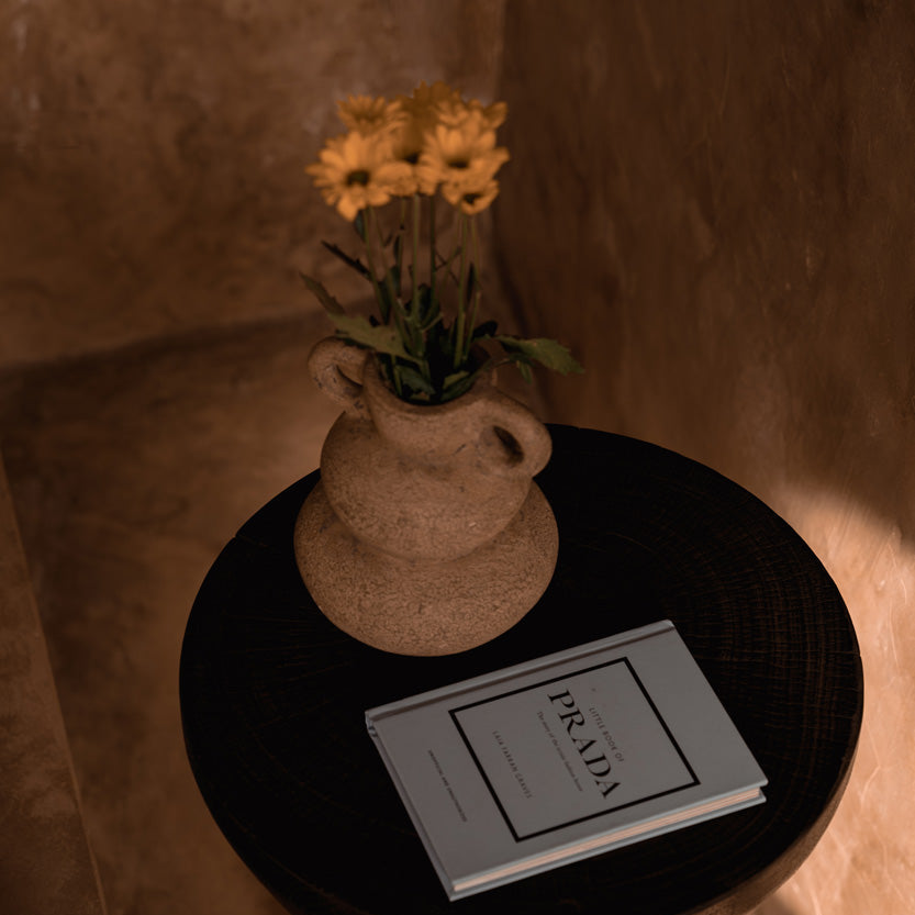 Small round table with a beige vase of flowers and a book on a soft, warm-toned background