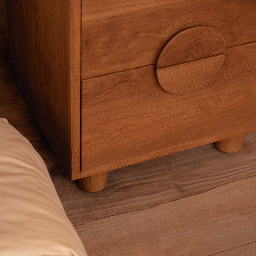 Wooden bedside table with a circular handle on a wooden floor.