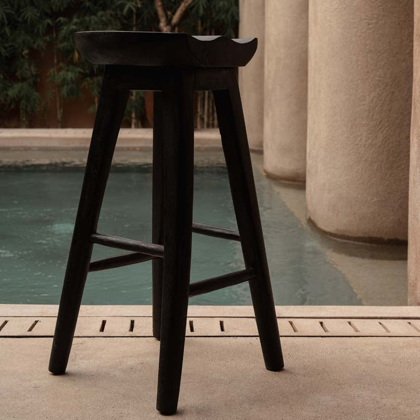 Black bar stool by a pool with architectural columns and greenery in the background