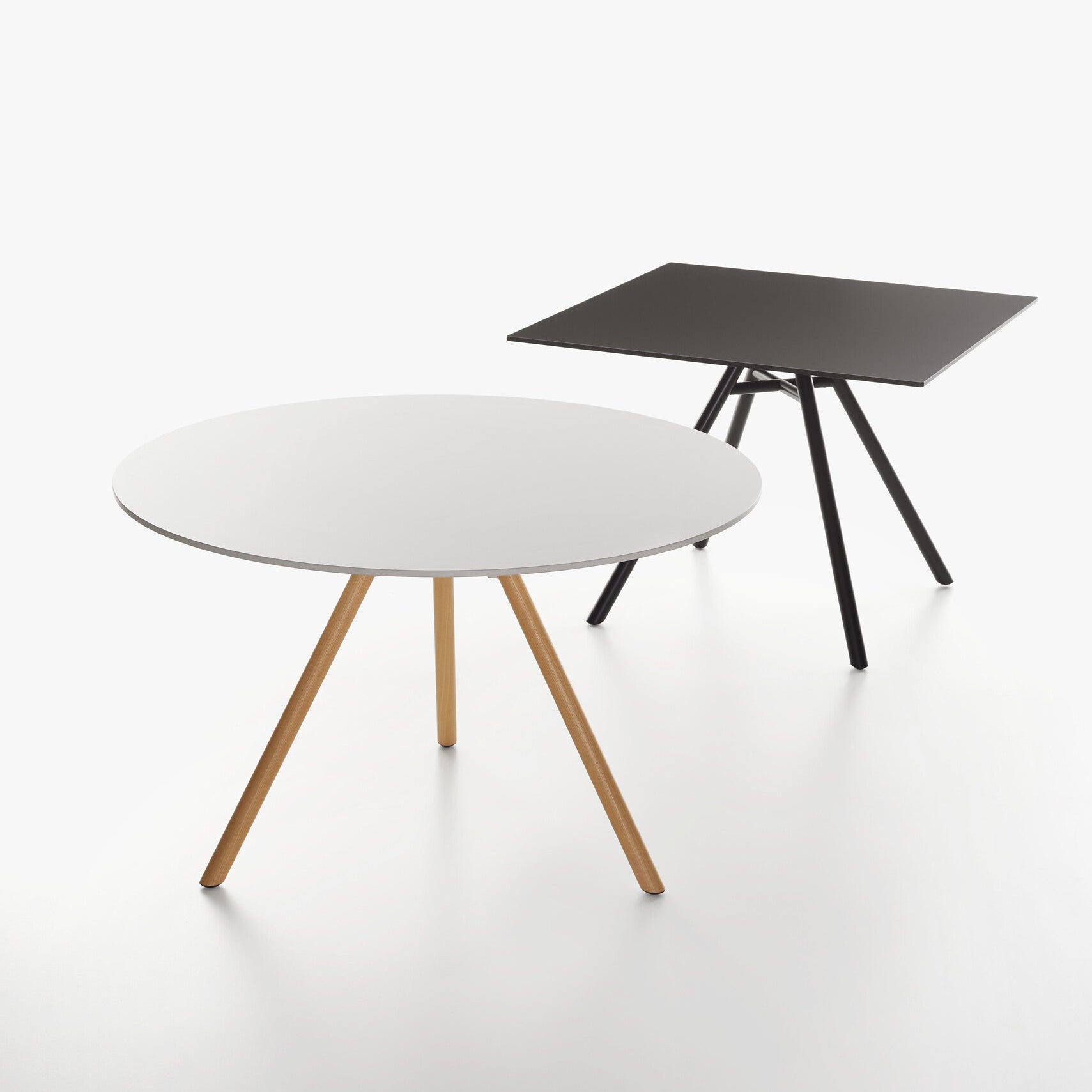 Two MART tables on a white studio background. The front table is round with a white top and the second is square table with black table top.